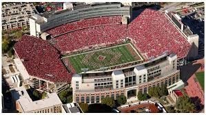 Aerial view of a large stadium filled with spectators in red, surrounding a green football field.