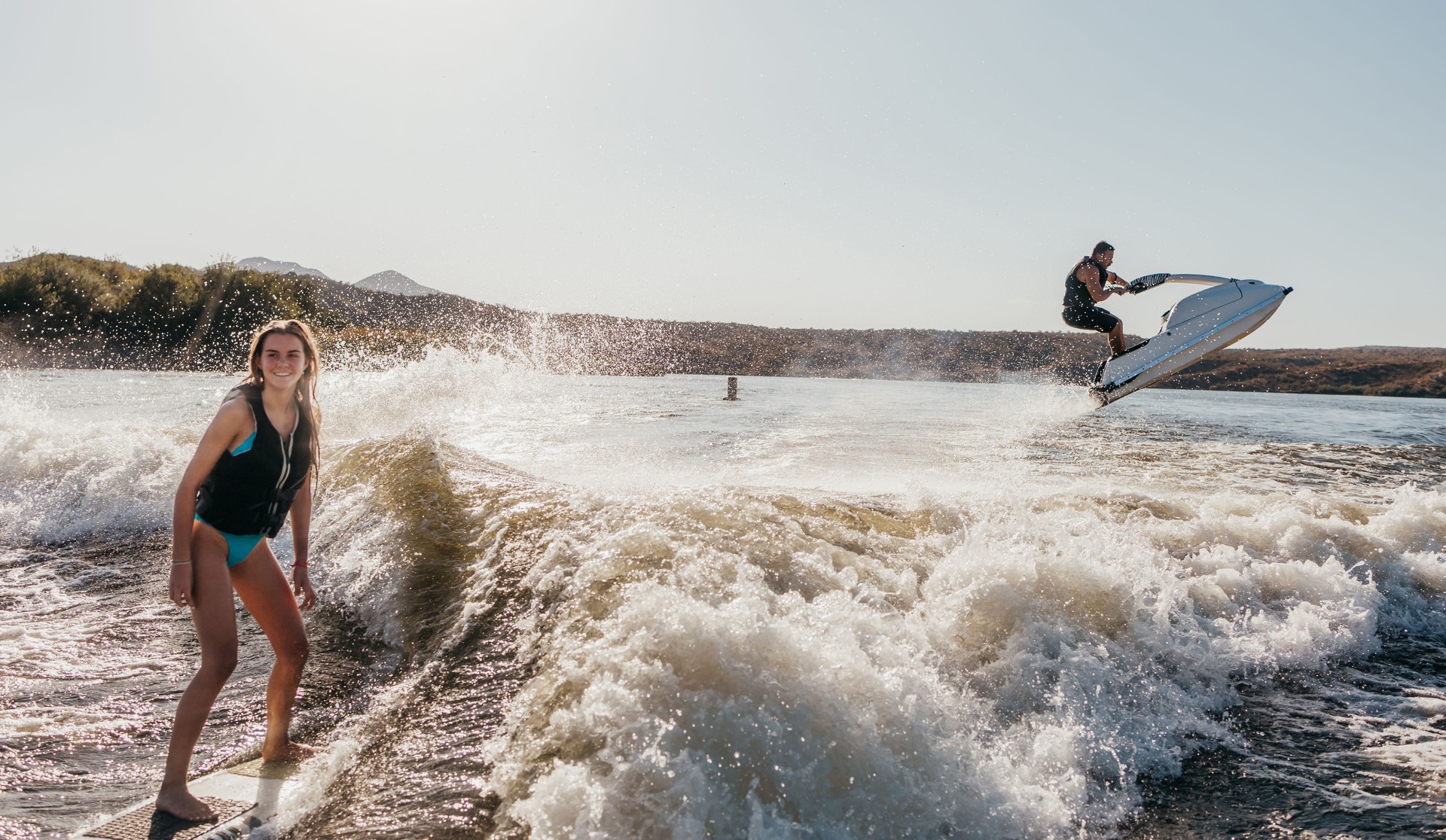 Teen girl wakeboards on lake and father jumps in air on PWC behind her